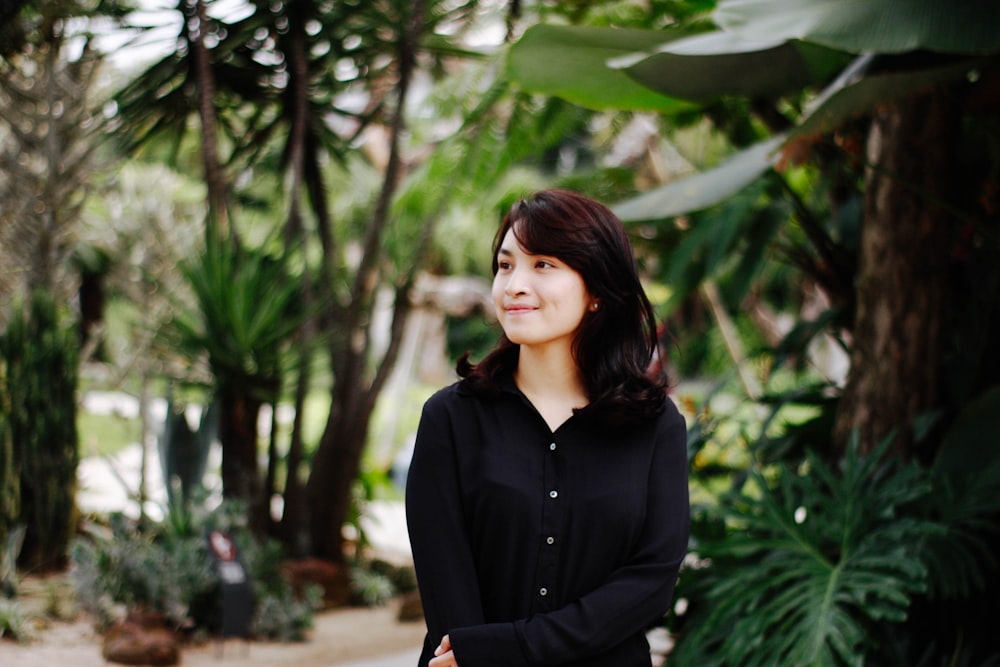 woman in black dress shirt standing near trees and smiling