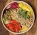 A vibrant salad bowl featuring a variety of fresh ingredients including chickpeas, pistachios, walnuts, sunflower seeds, sliced red peppers, yellow peppers, greens, and a portion of red pickled cabbage. These colorful ingredients are arranged artfully, creating a visually appealing and nutritious dish.