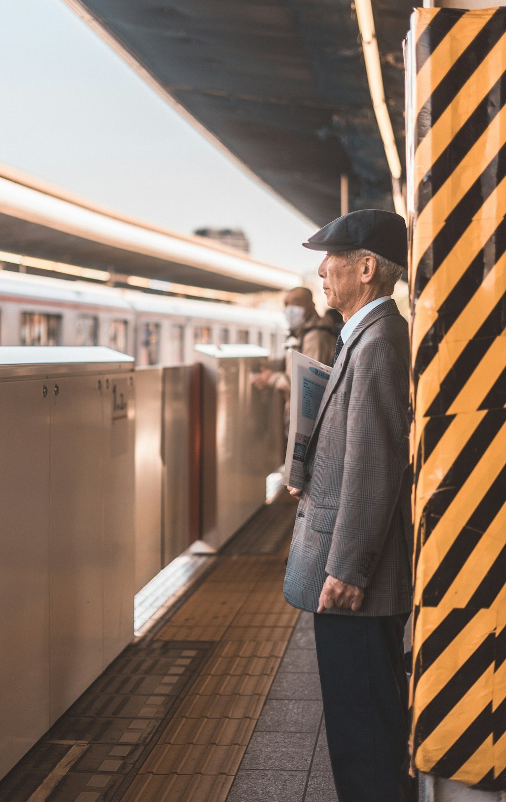 駅の黒と黄色の縞模様のポストのそばに立つグレーのスーツジャケットを着た男性