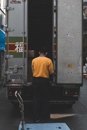 man in yellow sweater behind gray box truck