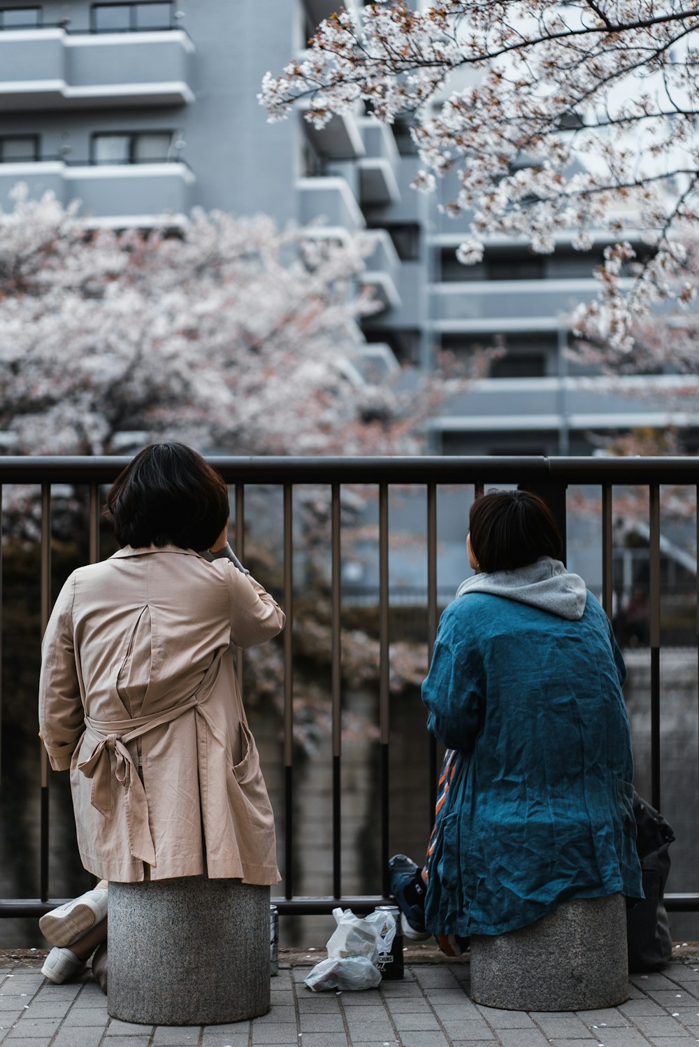 two woman sitting beside railing near building