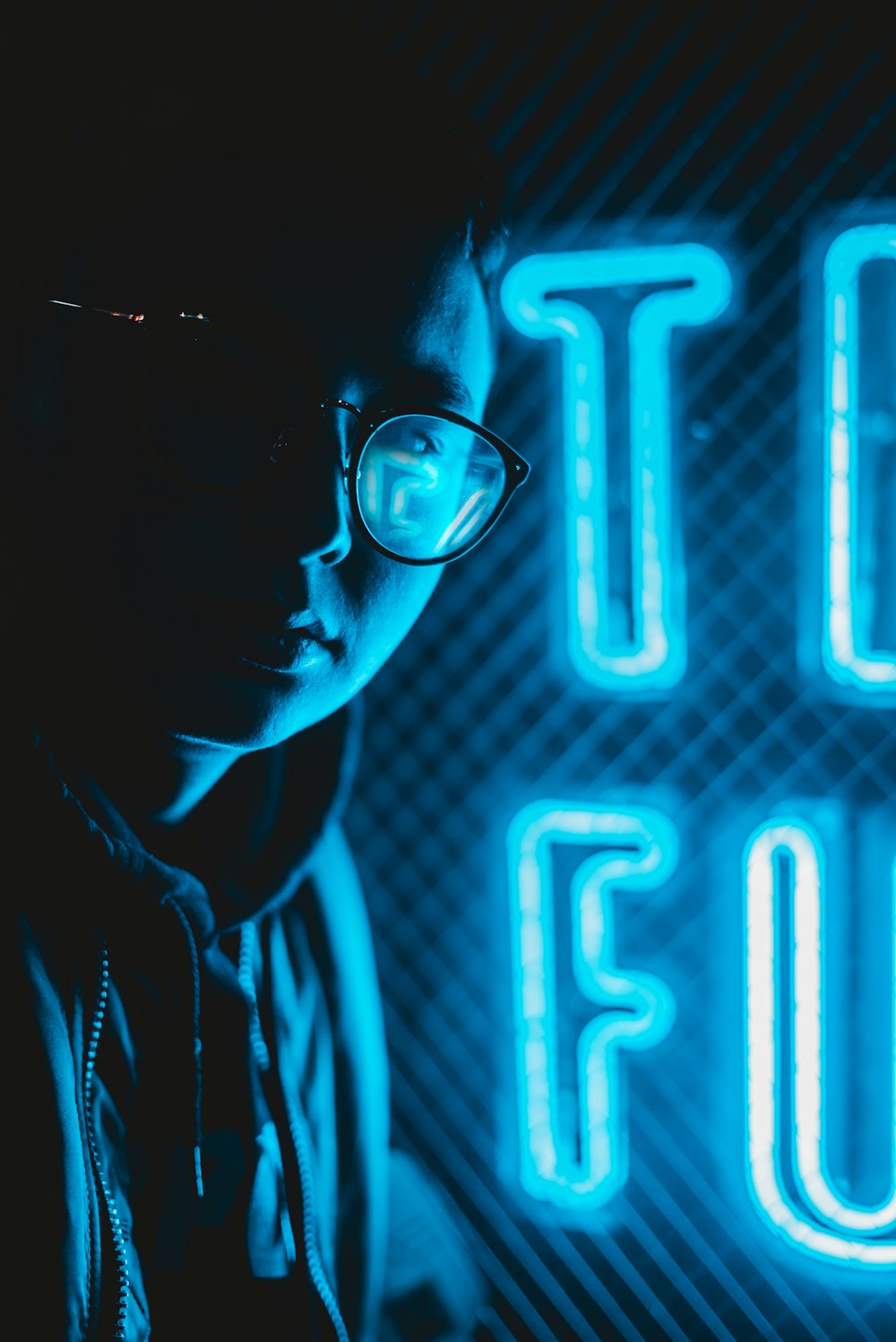 person in eyeglasses beside blue neon signage