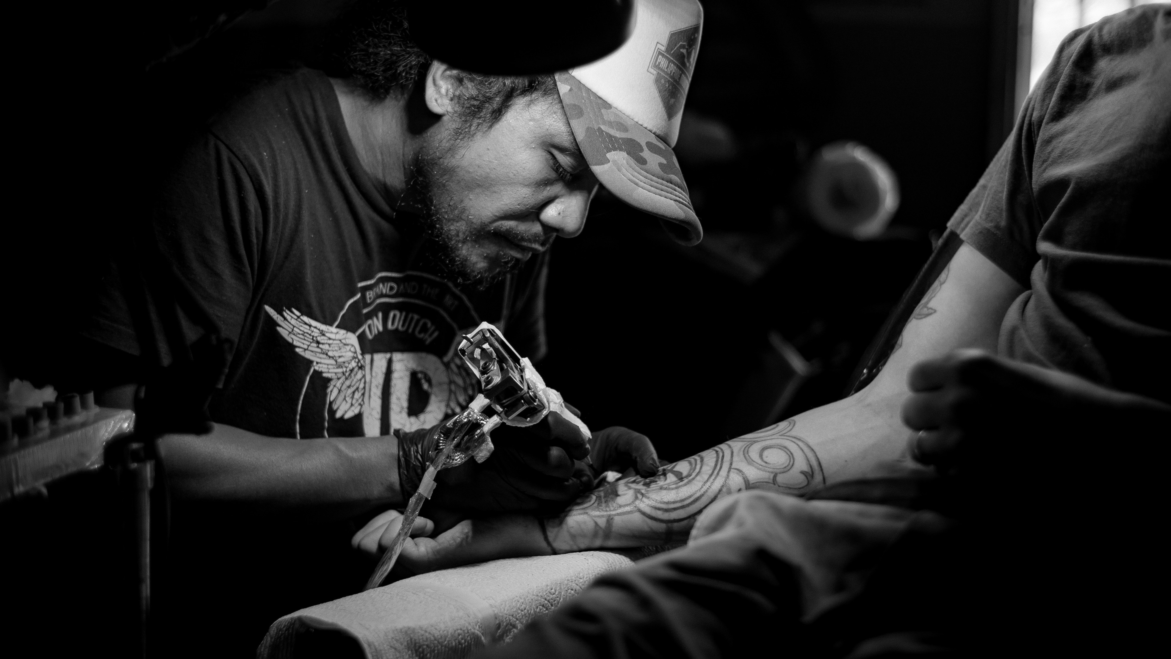 grayscale photo of man doing tattoo