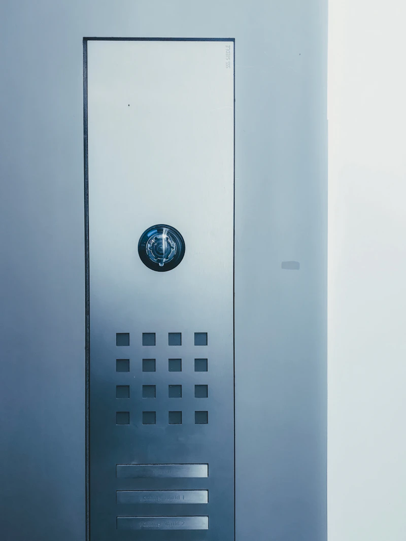 Wall-mounted video door phone panel with a camera lens and call buttons