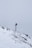 A snow-covered mountainous landscape with a metal pole topped by a small solar panel or device. A red and white windsock hangs from the pole, indicating wind direction. The surroundings are enveloped in fog, creating a serene and isolated atmosphere.