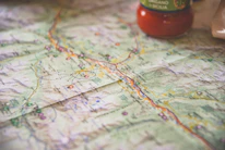 A detailed, folded map displays various geographical features and locations, with highlighted routes marked for travel. The print is clear, showing names and symbols. A jar of tomato sauce is partially visible in the corner, indicating a kitchen or dining setting.