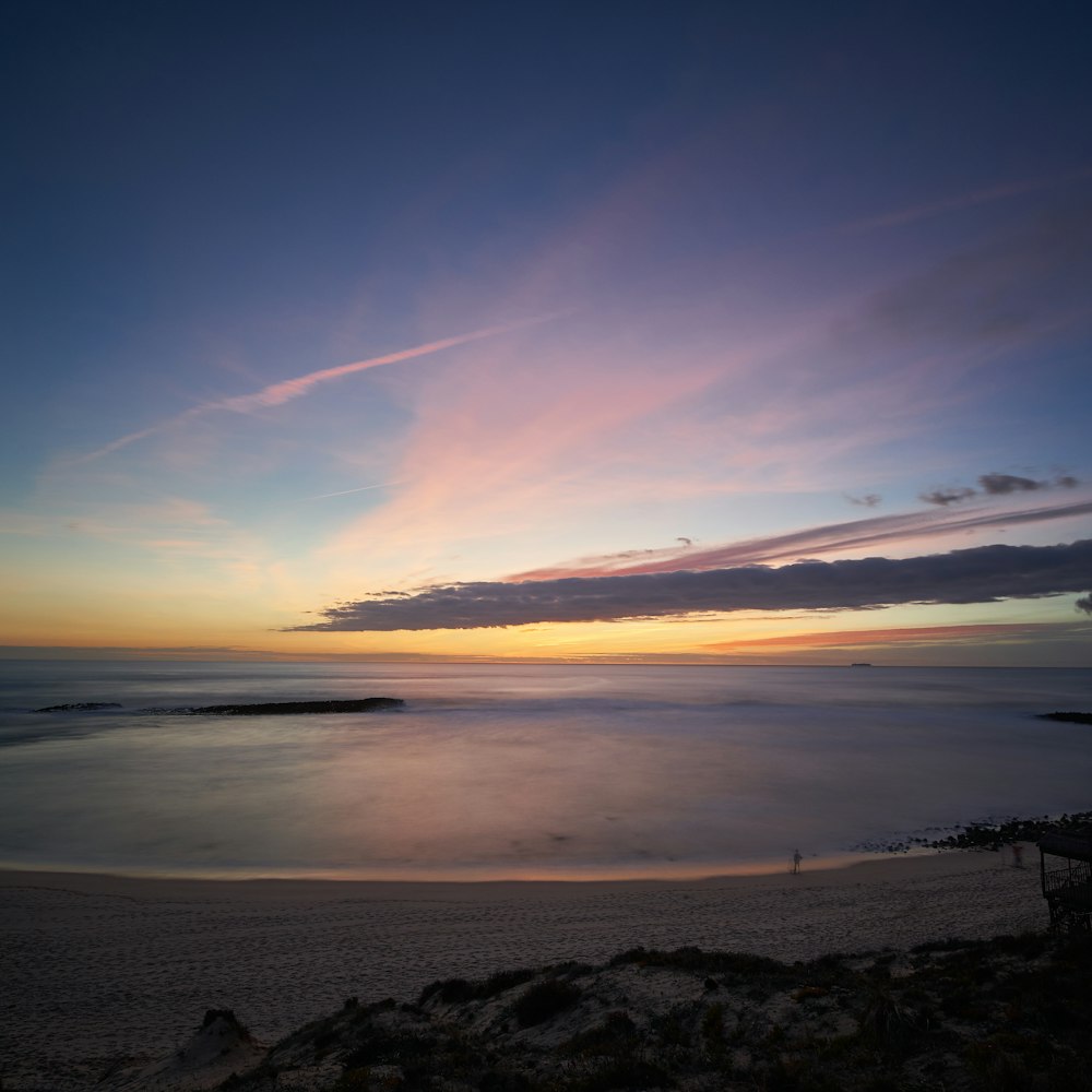 grass on shore under cloudy sky during sunrise