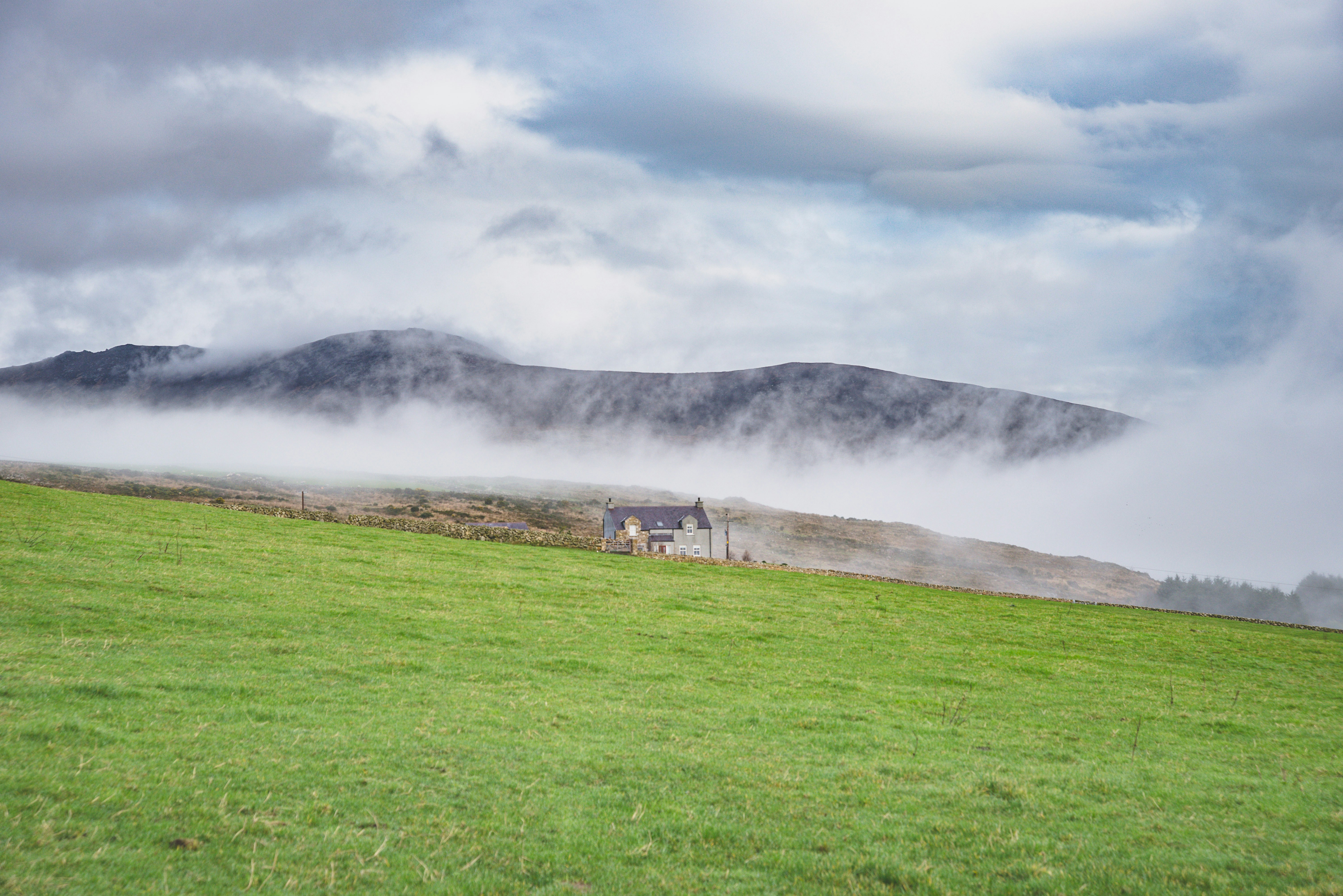 grass field near mountain covered by clouds