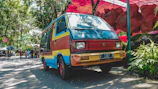 A fleet of diverse vehicles adorned with colorful Mobiluz stickers parked outside a shopping mall on a sunny day.
