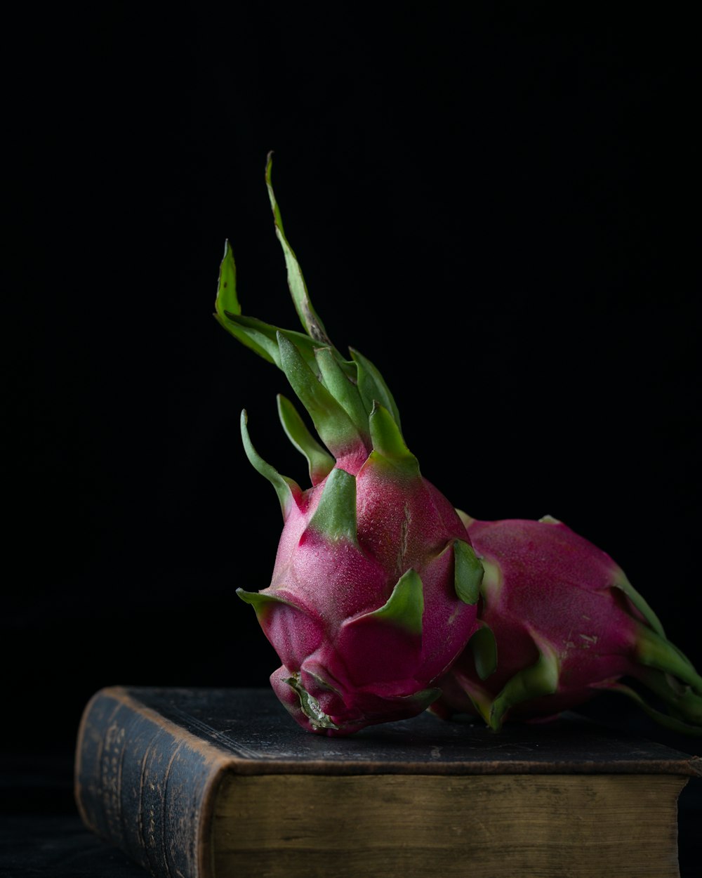 two pink-and-green dragon fruits on hardbound book