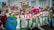 A large group of people, mostly young individuals, are participating in a climate march. They hold banners and signs with slogans advocating for environmental action. One prominent banner reads 'March for Climate' with a drawing of the Earth. Some participants are wearing colorful clothing, and one person holds a bright pink umbrella.