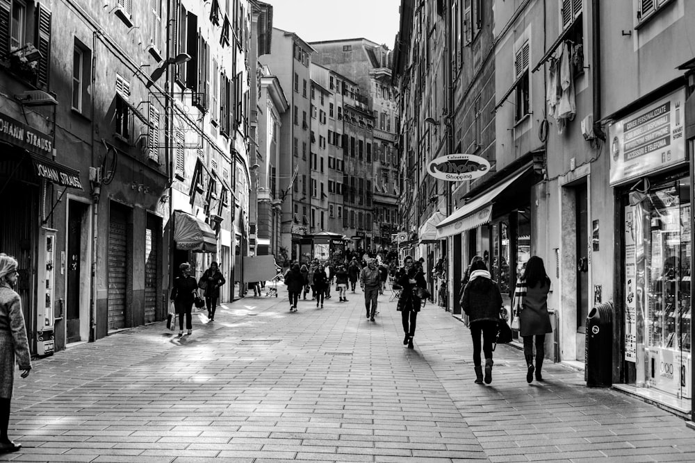 grayscale photo of people walking between buildings during daytime