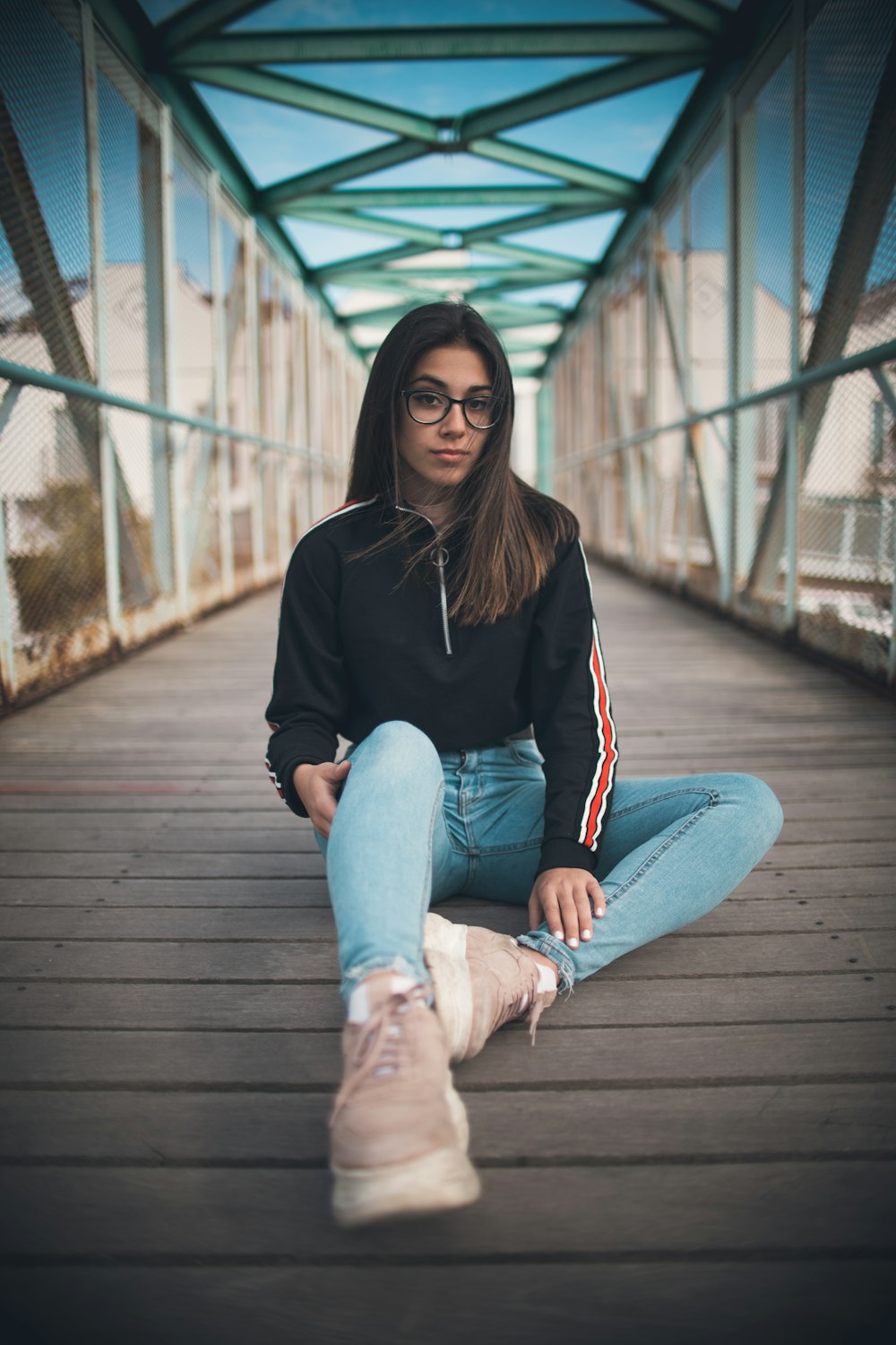 woman wearing jacket and denim jeans sitting on brown bridge
