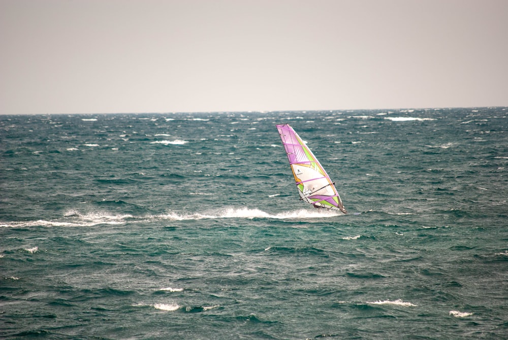 pink, white, and yellow sailboat on body of water