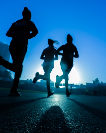 silhouette of three women running on grey concrete road