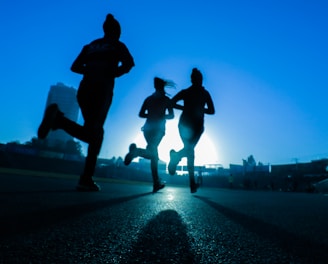 silhouette of three women running on grey concrete road