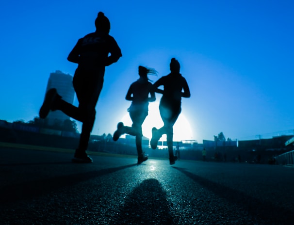 silhouette of three women running on grey concrete road