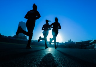 silhouette of three women running on grey concrete road