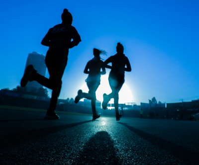 silhouette of three women running on grey concrete road