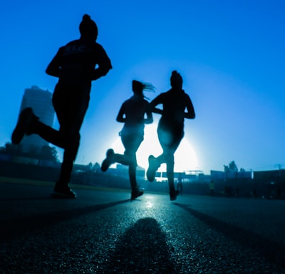 silhouette of three women running on grey concrete road