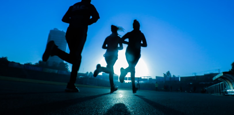 silhouette of three women running on grey concrete road