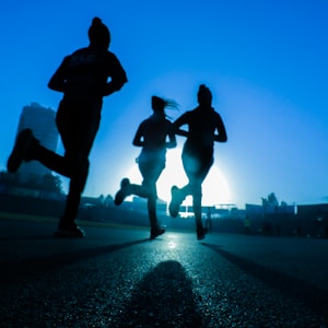 silhouette of three women running on grey concrete road