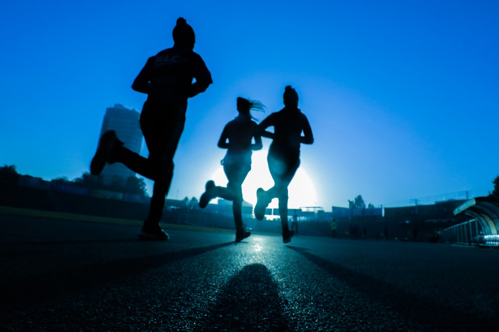 silhouette of three women running on grey concrete road