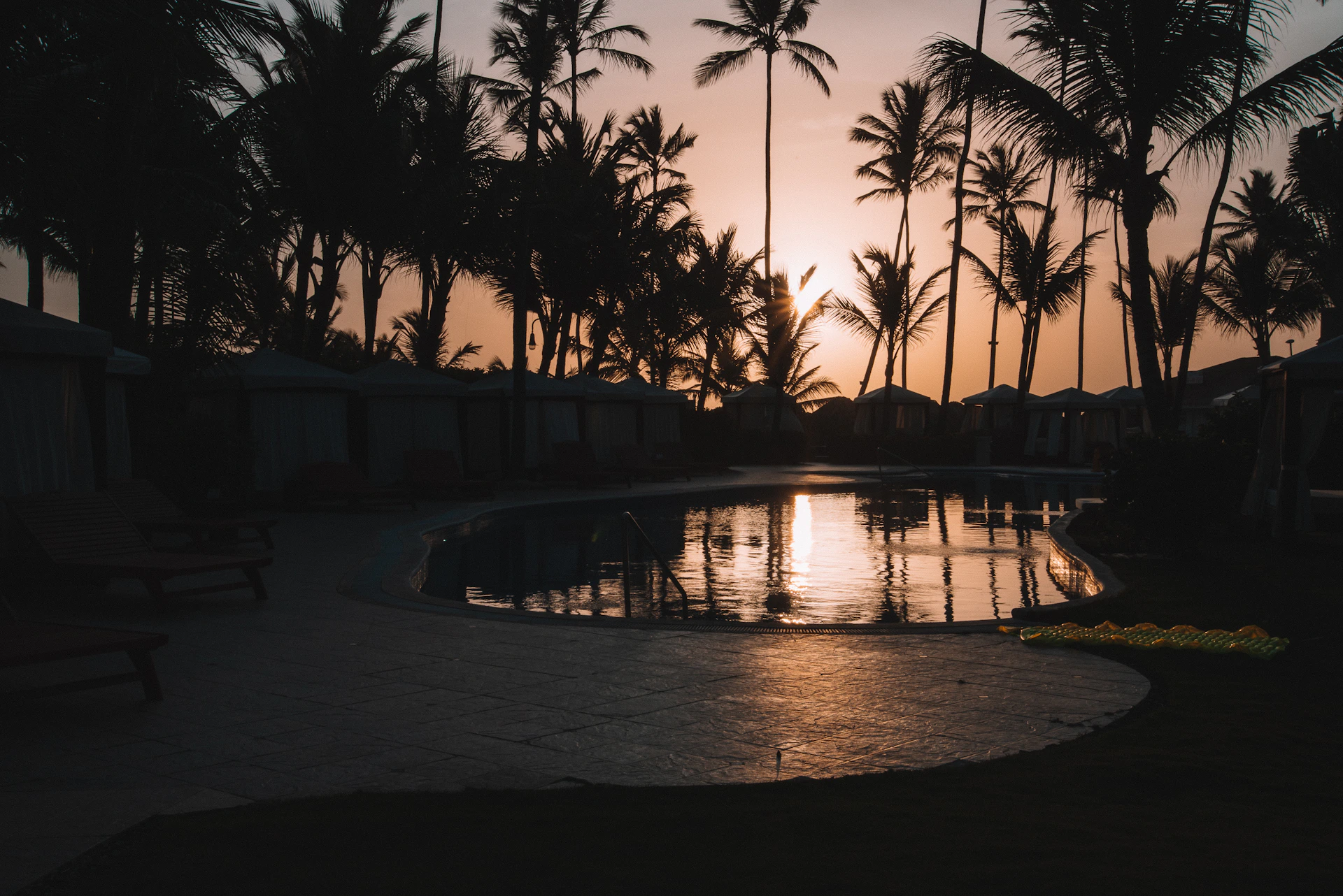 A peaceful oasis scene with palm trees and a calm water pool reflecting the golden hues of a desert sunset.