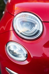 A close-up view of two car headlights on a red vehicle, showcasing a modern and sleek design with a shiny, reflective surface.