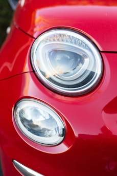 A close-up view of two car headlights on a red vehicle, showcasing a modern and sleek design with a shiny, reflective surface.