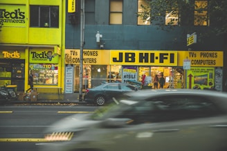 A bustling Baghdad street with company trucks and electronic devices displayed in a shop window.