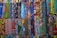A vibrant collection of various African wax print fabrics, neatly arranged in rows. Each piece features a unique pattern, including geometric shapes, swirls, and florals, in a wide array of colors like blue, orange, yellow, and green.