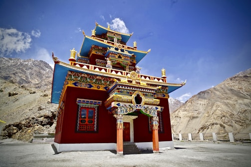 A colorful Buddhist monastery nestled among lush green hills under a clear blue sky.