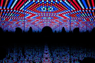 A visually striking play of vibrant LED lights forming geometric patterns in red, blue, and white, creating a tunnel-like illusion with repetitive reflections.
