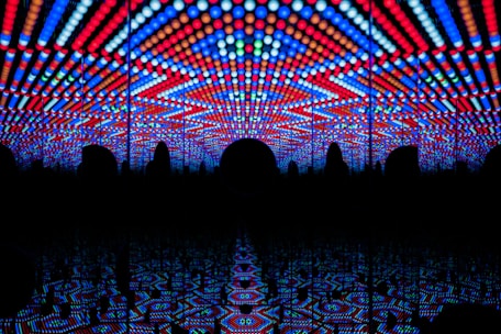 A visually striking play of vibrant LED lights forming geometric patterns in red, blue, and white, creating a tunnel-like illusion with repetitive reflections.