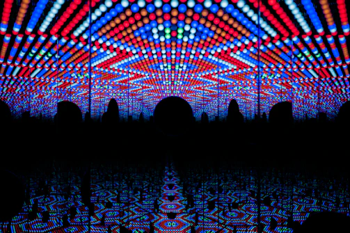 A visually striking play of vibrant LED lights forming geometric patterns in red, blue, and white, creating a tunnel-like illusion with repetitive reflections.