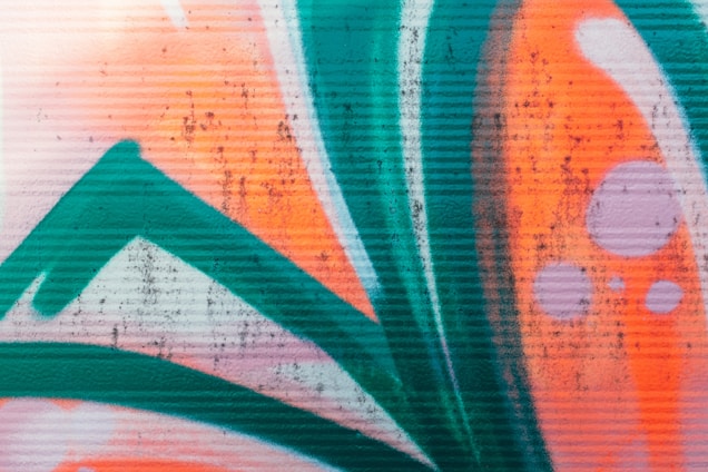Bold, vibrant graffiti featuring abstract shapes and lines painted in bright orange, teal, and white with some purple accents, creating an eye-catching urban art piece.