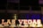 Bold, illuminated letters spell out 'Las Vegas' against a dark background, with vibrant colors and a blurred backdrop suggesting a lively, bustling environment.