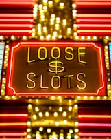 Bright neon lights display the words 'Loose Slots' with a dollar sign in the center. The sign is outlined with bulbs, creating a vibrant and flashy effect typical of a casino or entertainment venue.