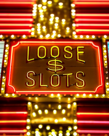 Bright neon lights display the words 'Loose Slots' with a dollar sign in the center. The sign is outlined with bulbs, creating a vibrant and flashy effect typical of a casino or entertainment venue.