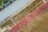 An aerial view of a sports complex featuring a running track and a grassy field. The tracks are red and situated next to a large building. There are several people scattered across the area, some on the track and others near the building. The surroundings include trees and geometric pathways, adding structure to the scene.