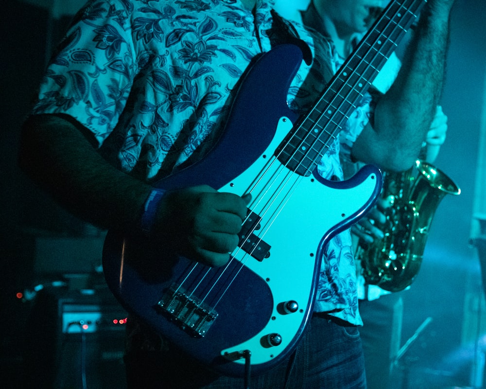 man holding blue and white 4-string bass guitar