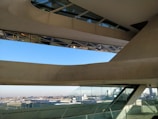 An architectural space featuring large, angular concrete and glass structures with an expansive view of a cityscape in the background. The design includes slanted windows and geometric shapes, creating a modern and innovative look.