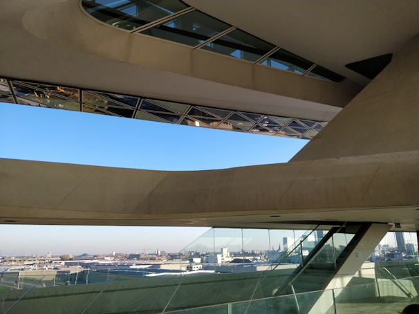 An architectural space featuring large, angular concrete and glass structures with an expansive view of a cityscape in the background. The design includes slanted windows and geometric shapes, creating a modern and innovative look.
