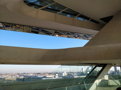 An architectural space featuring large, angular concrete and glass structures with an expansive view of a cityscape in the background. The design includes slanted windows and geometric shapes, creating a modern and innovative look.