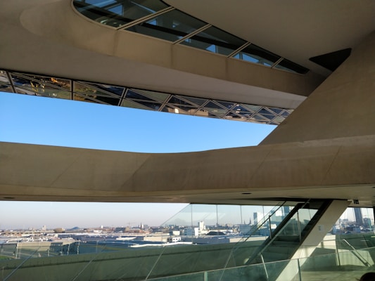 An architectural space featuring large, angular concrete and glass structures with an expansive view of a cityscape in the background. The design includes slanted windows and geometric shapes, creating a modern and innovative look.