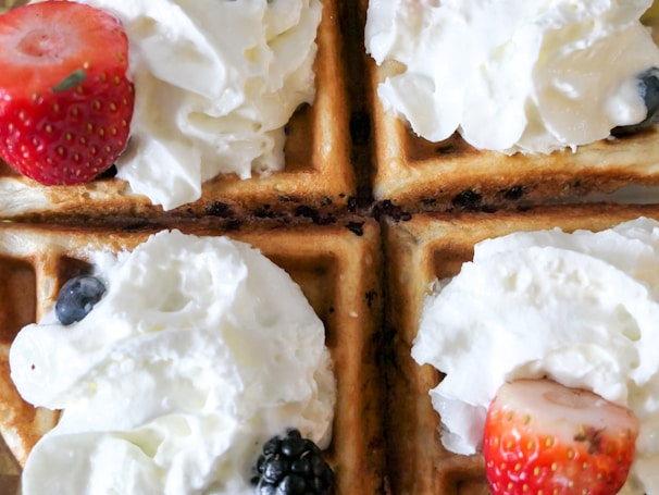 Golden brown waffles topped with generous dollops of whipped cream and fresh berries including strawberries, blueberries, and blackberries.