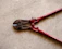 A pair of red bolt cutters rests on a concrete surface. The metal jaws and pivot mechanism are visible, showcasing the tool's sturdy construction.