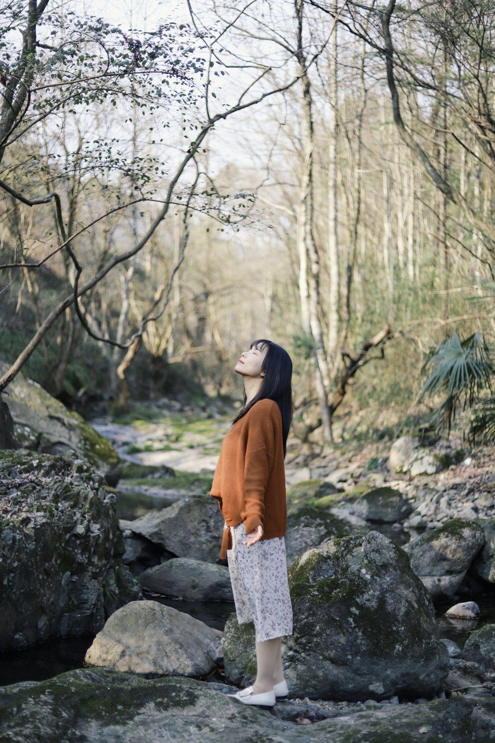 woman standing at the rock in the middle of the forest