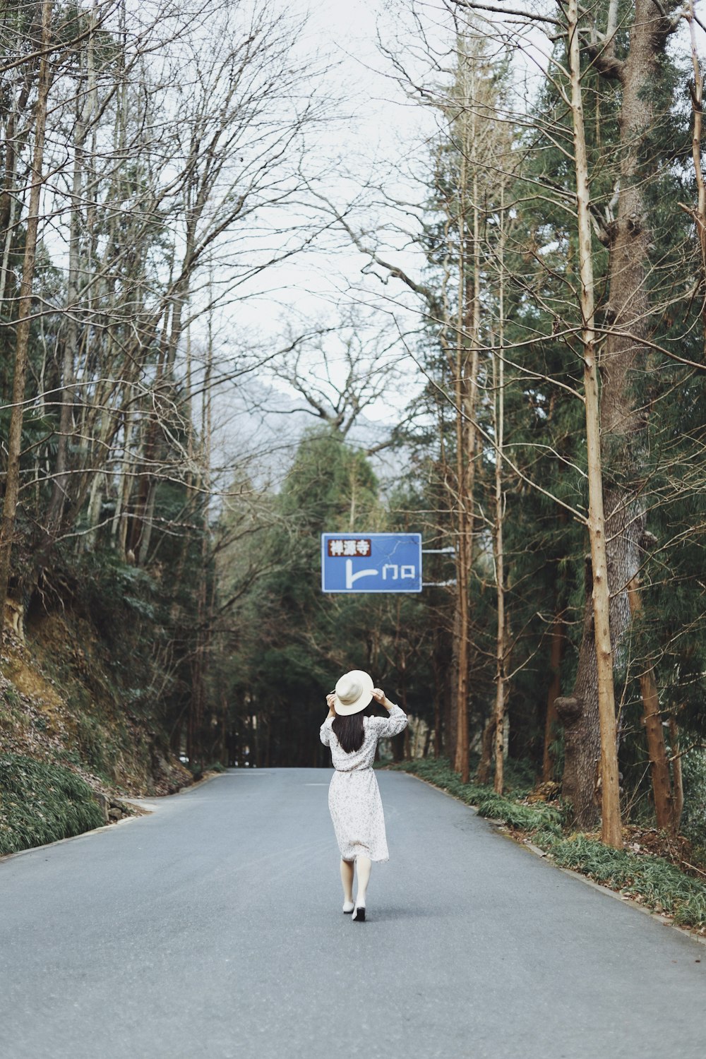 woman walking on road between bare trees